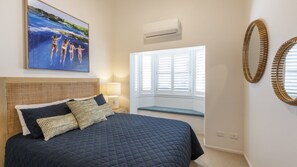 Una camera da letto con un letto, una finestra con persiane, un condizionatore d'aria e un quadro appeso al muro.
