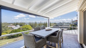 A balcony with a table and chairs, overlooking a residential area and a body of water.