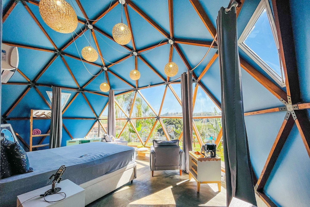 A modern, geometric interior with a large bed, seating area, and a view of greenery outside.