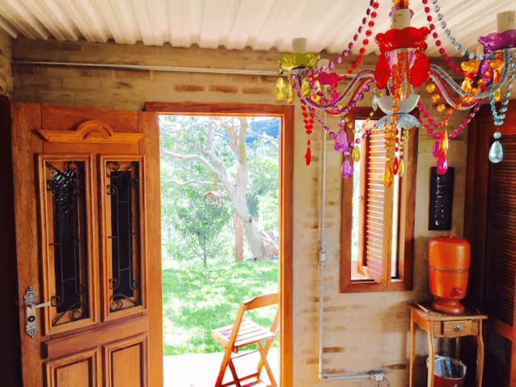 Um quarto com porta de madeira, janela com persianas, uma cadeira e um objeto decorativo pendurado.