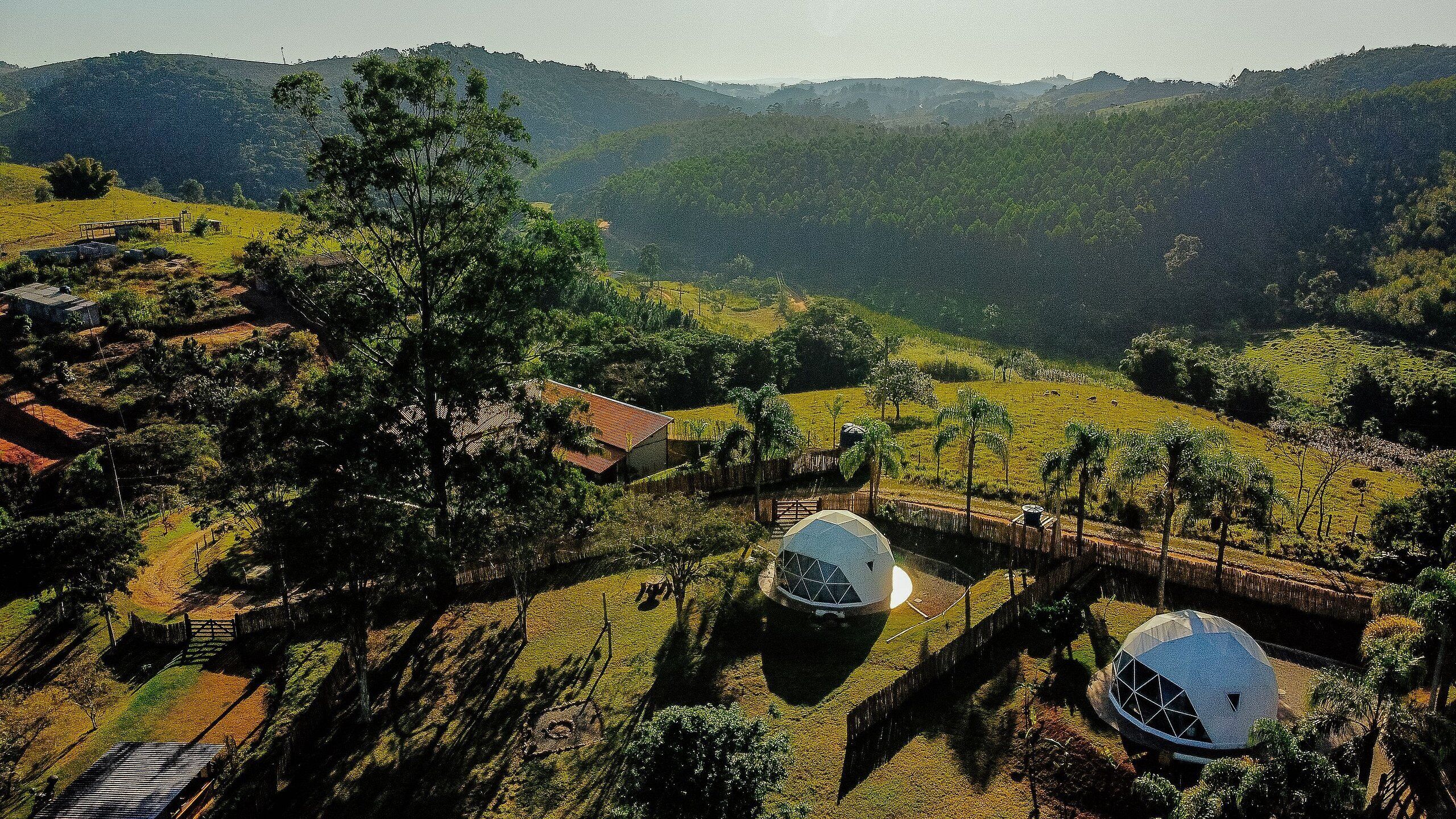 Paisaje rural con dos estructuras esféricas, un puente de madera y un pequeño edificio.