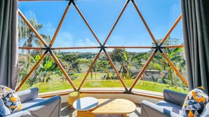 A room with a large glass window, a wooden table, two sofas, and a patterned cushion. - Rua José Joaquim Nogueira (Santa Branca)