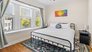 A bedroom with a bed, a nightstand, a ceiling fan, and a window with curtains. - North Center Chicago - Walkable - Transit Accessible - King & Queen Beds (Chicago)