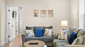 A living room with a grey sofa, a coffee table, and a lamp. There are three wall art pieces above the sofa. - North Center Chicago - Walkable - Transit Accessible - King & Queen Beds (Chicago)
