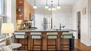 A modern kitchen with a central island, bar stools, wooden cabinets, stainless steel appliances, and pendant lighting. - North Center Chicago - Walkable - Transit Accessible - King & Queen Beds (Chicago)