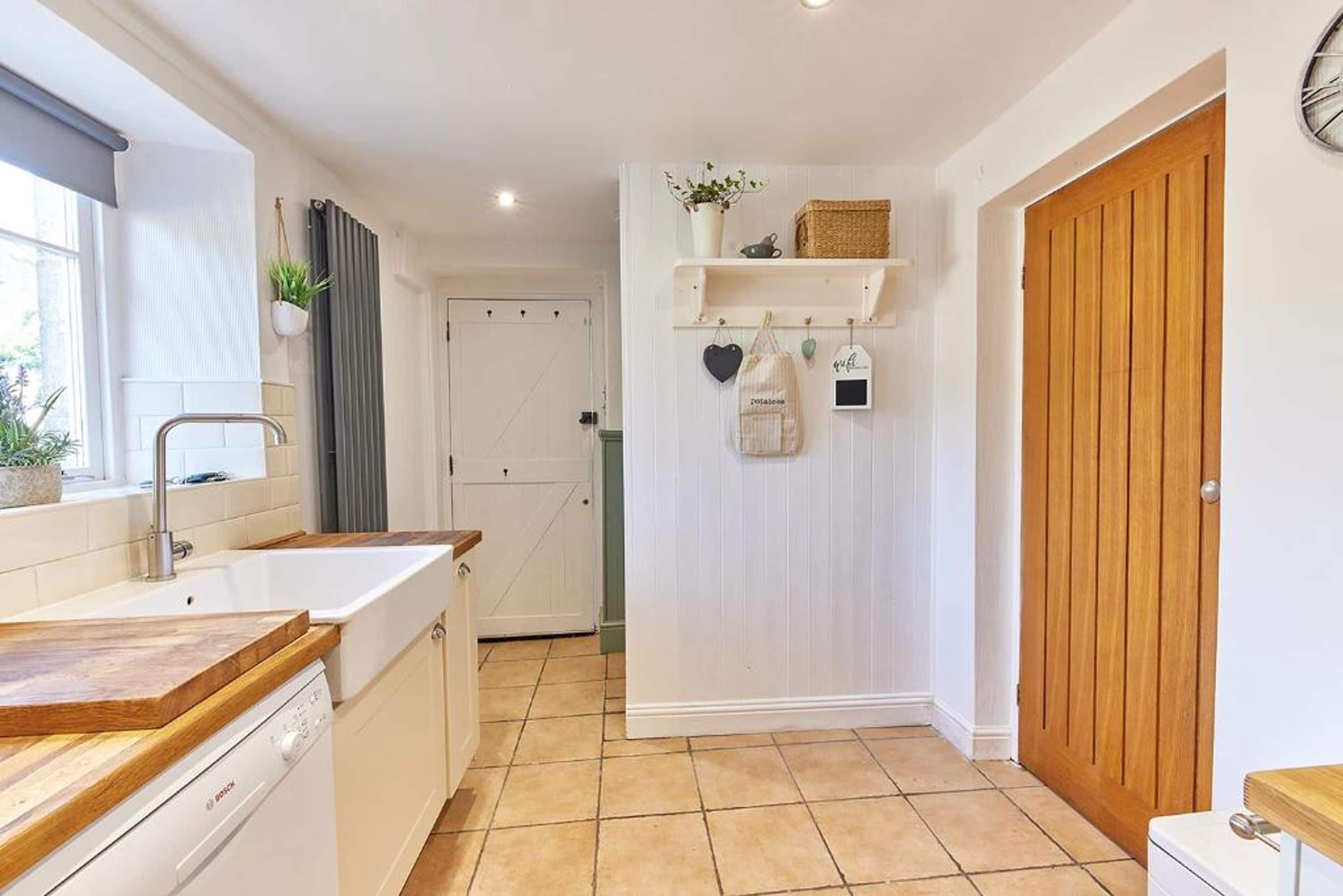 A compact kitchen with a Bosch dishwasher, a window with blinds, a wooden door, and a tiled floor.