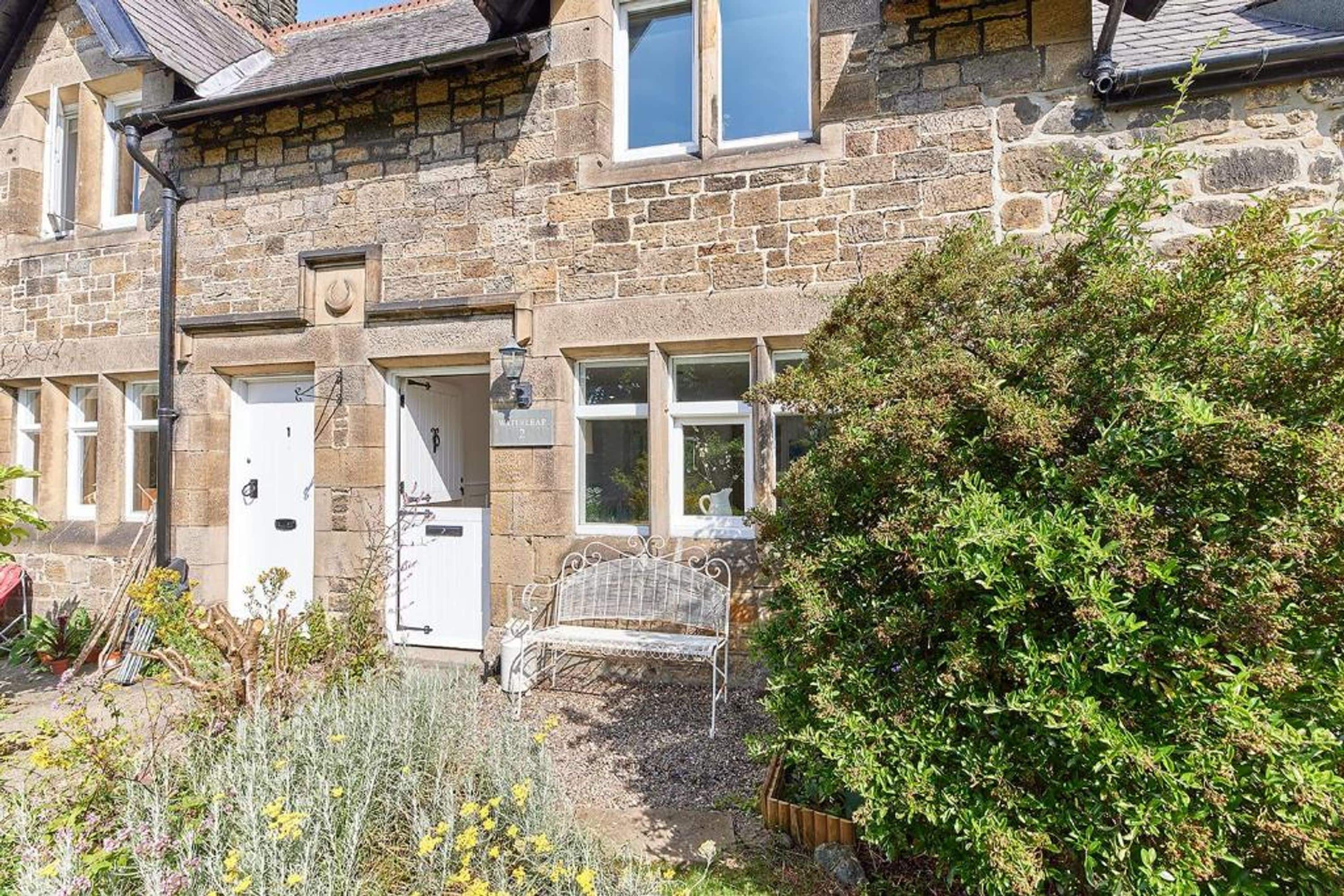 A stone house with a white door, windows, and a bench in the garden.