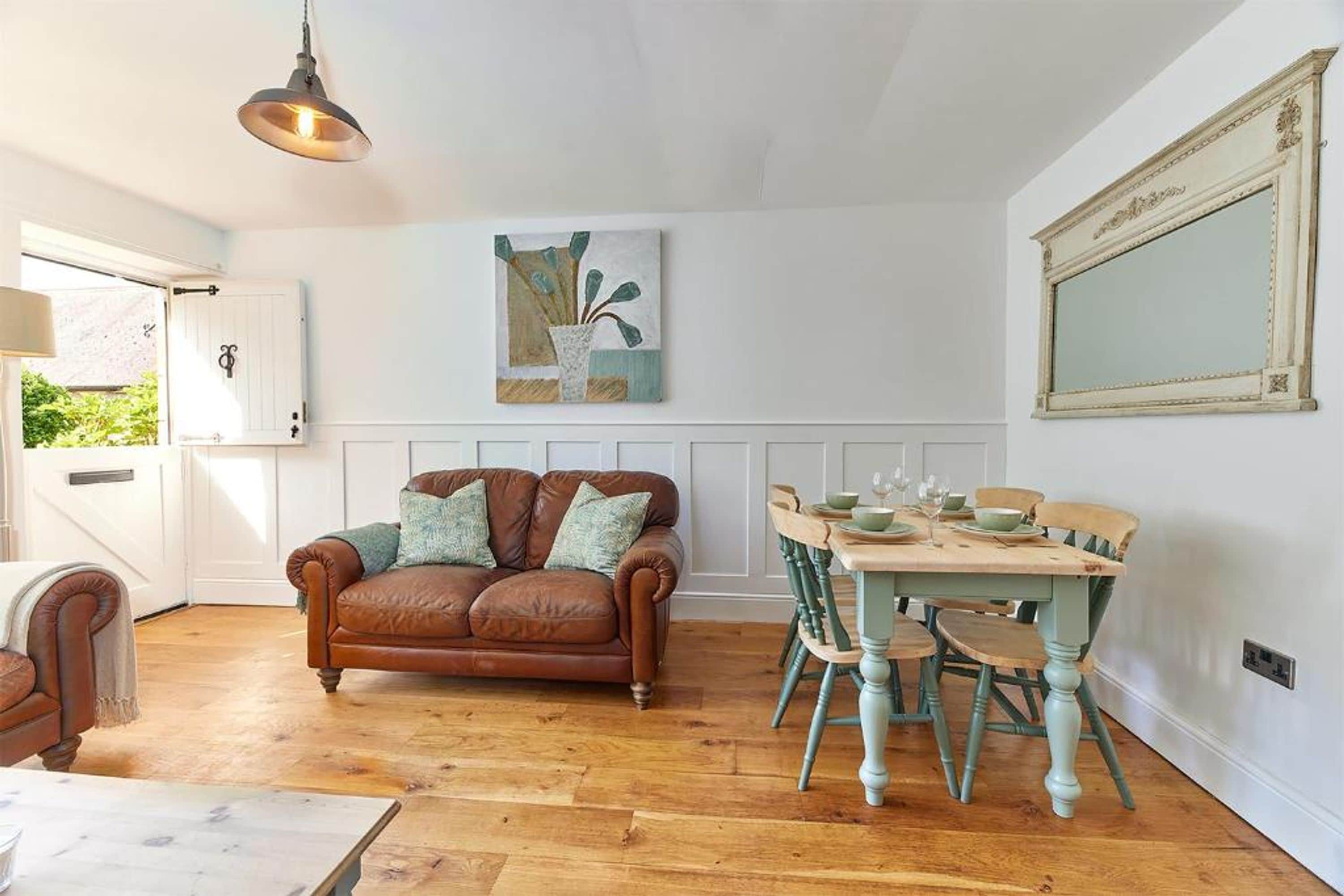Et hyggeligt rum med en brun lædersofa, et spisebord med stole og en hængende lampe.