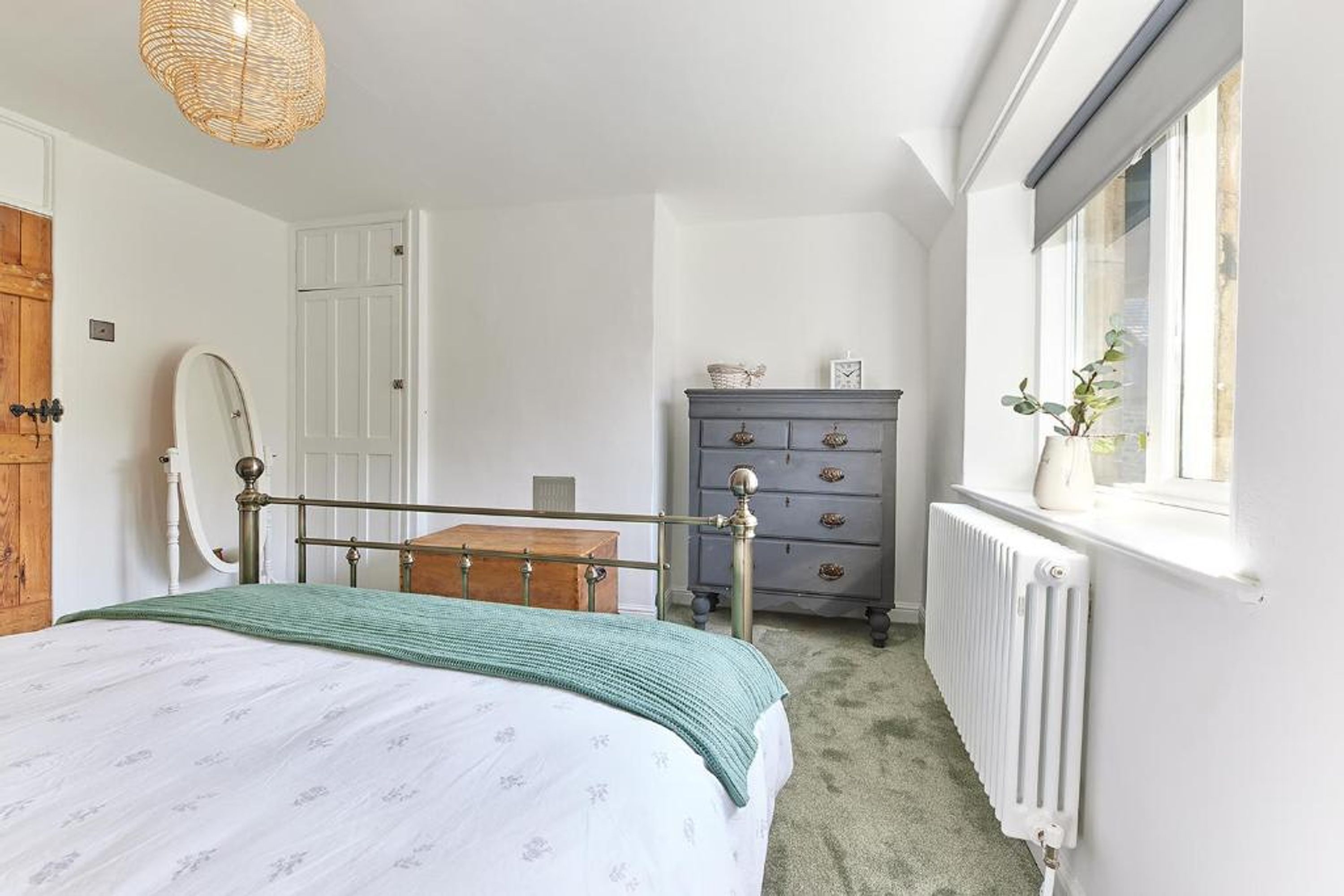 Un dormitorio con cama, cómoda, radiador y ventana con planta.