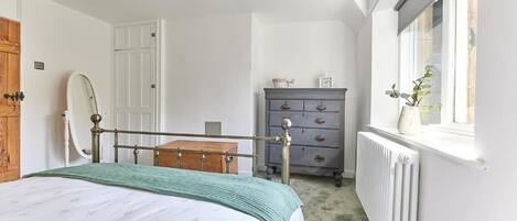 Un dormitorio con cama, cómoda, radiador y ventana con planta.