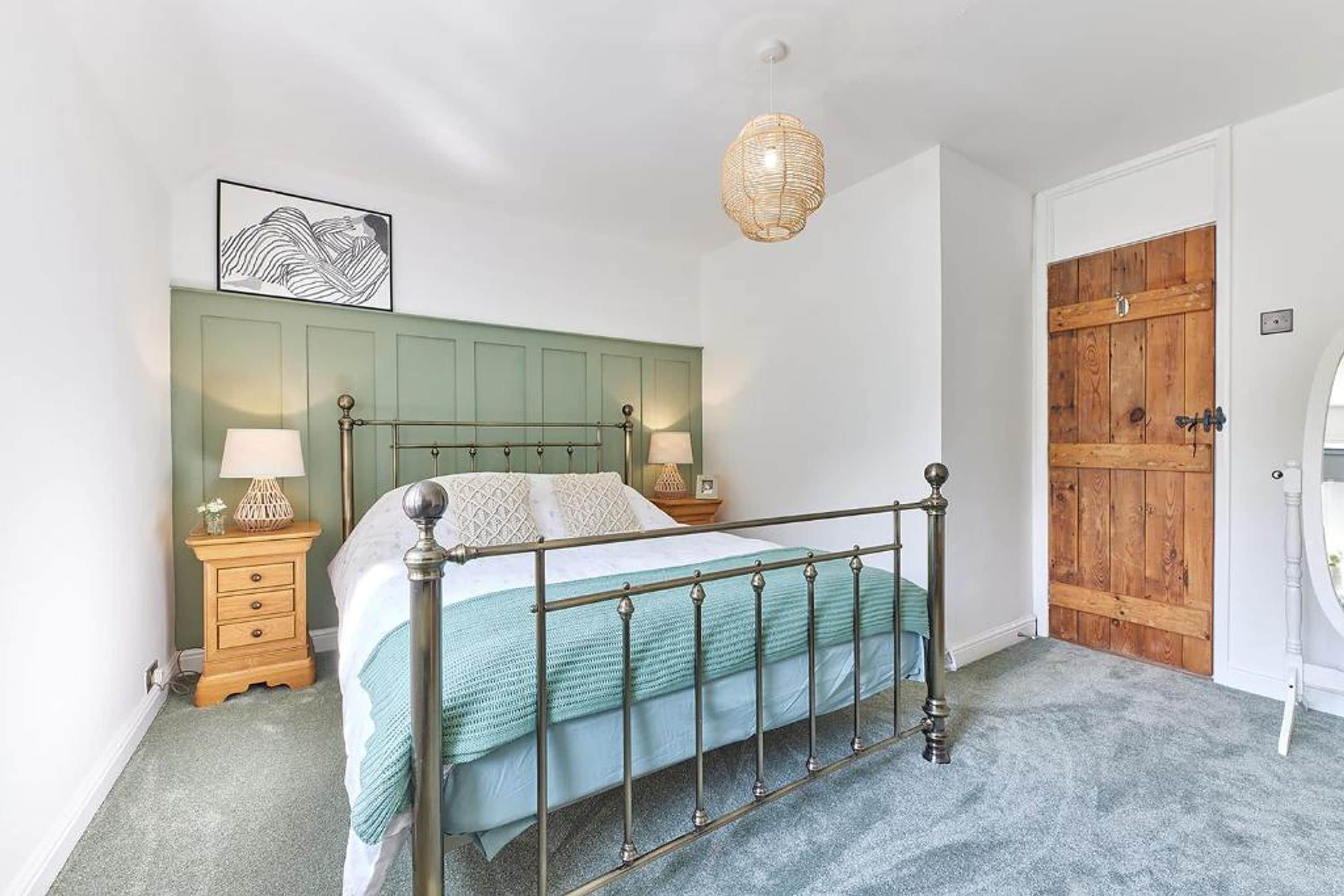 A bedroom with a metal-framed bed, a green headboard, a wooden door, and a hanging light fixture.