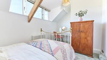 A bedroom with a bed, a wooden wardrobe, a desk with a chair, and a window.