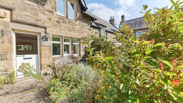 A stone house with a front door, windows, and a garden with various plants.