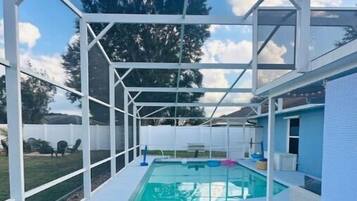 Un espace extérieur abrité comprenant une piscine, deux chaises longues et une petite table agrémentée d’une plante.