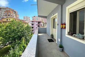Varanda estreita com vista para edifícios vizinhos, uma porta e uma janela com extintores.