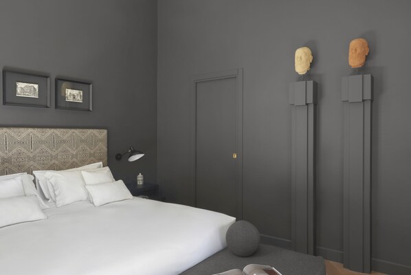 Un dormitorio moderno con una cama grande, cabecera con diseño geométrico, dos cuadros en la pared, una mesita de noche con lámpara y una puerta con un pequeño ventanal.