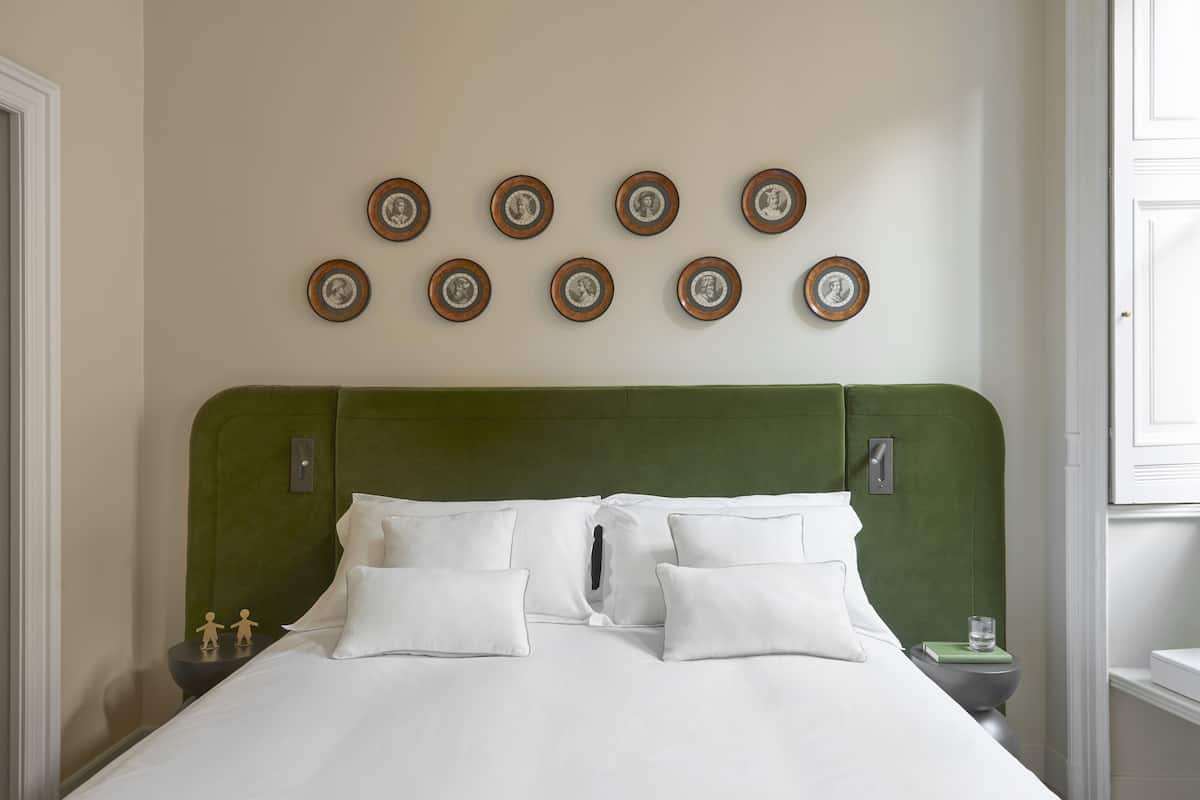 A neatly made bed with white linens, a green upholstered headboard, and a series of framed pictures on the wall.