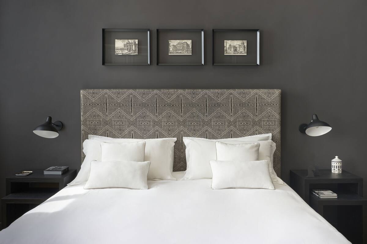 A neatly made bed with white linens and pillows, a patterned headboard, and three framed pictures on the wall.