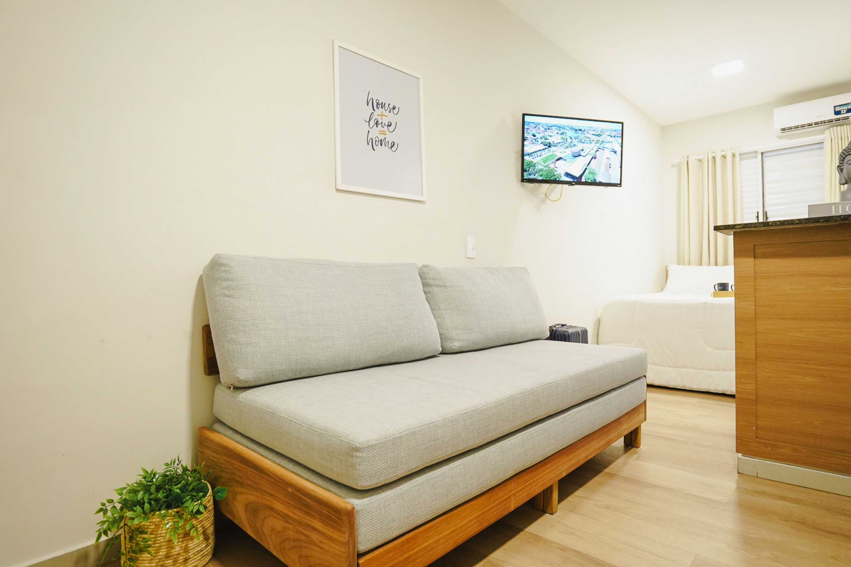 Un salon minimaliste avec un canapé gris, un meuble en bois, un téléviseur et une citation encadrée accrochée au mur.