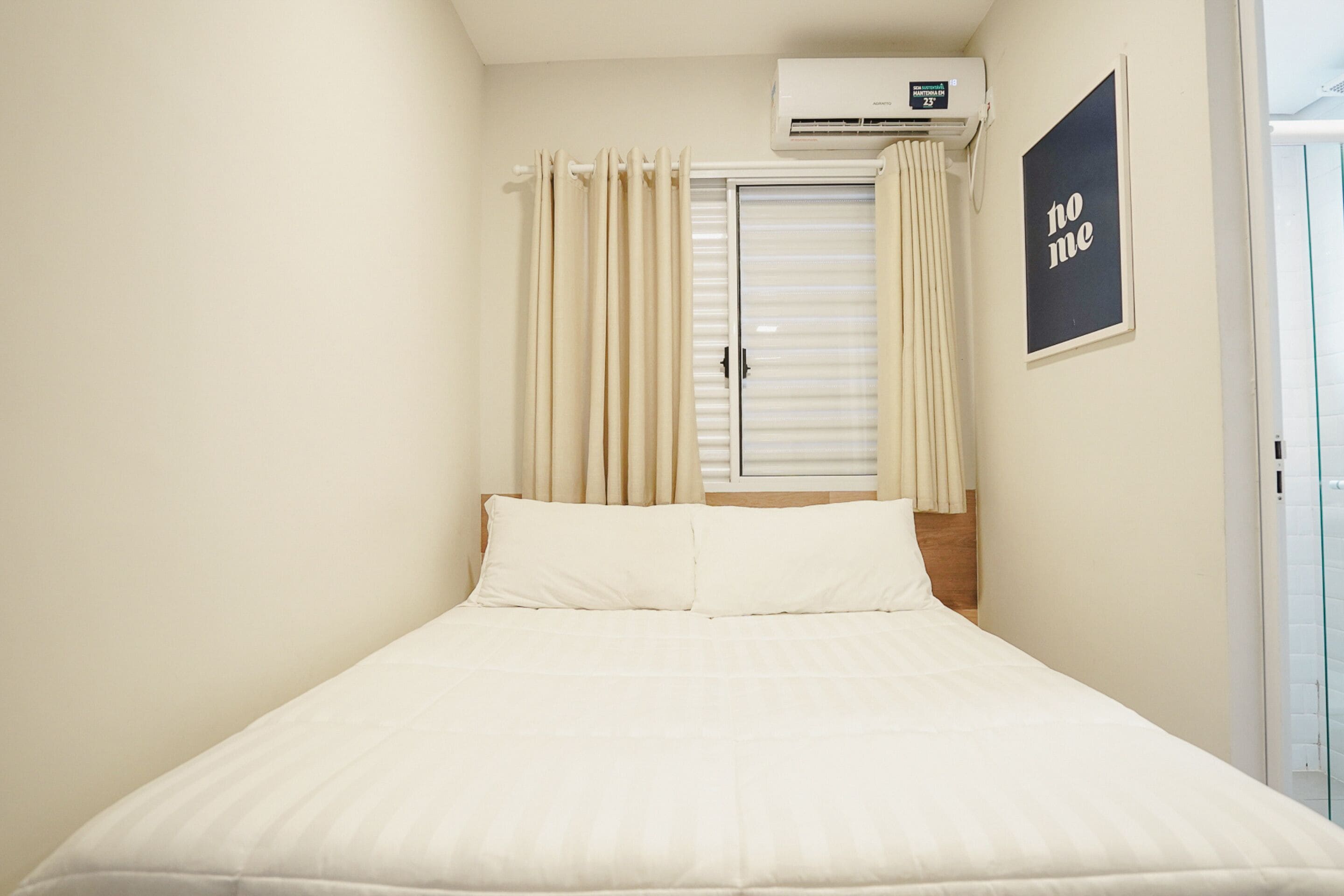 A bedroom with a bed, curtains, an air conditioning unit, and a 'no me' sign on the wall.