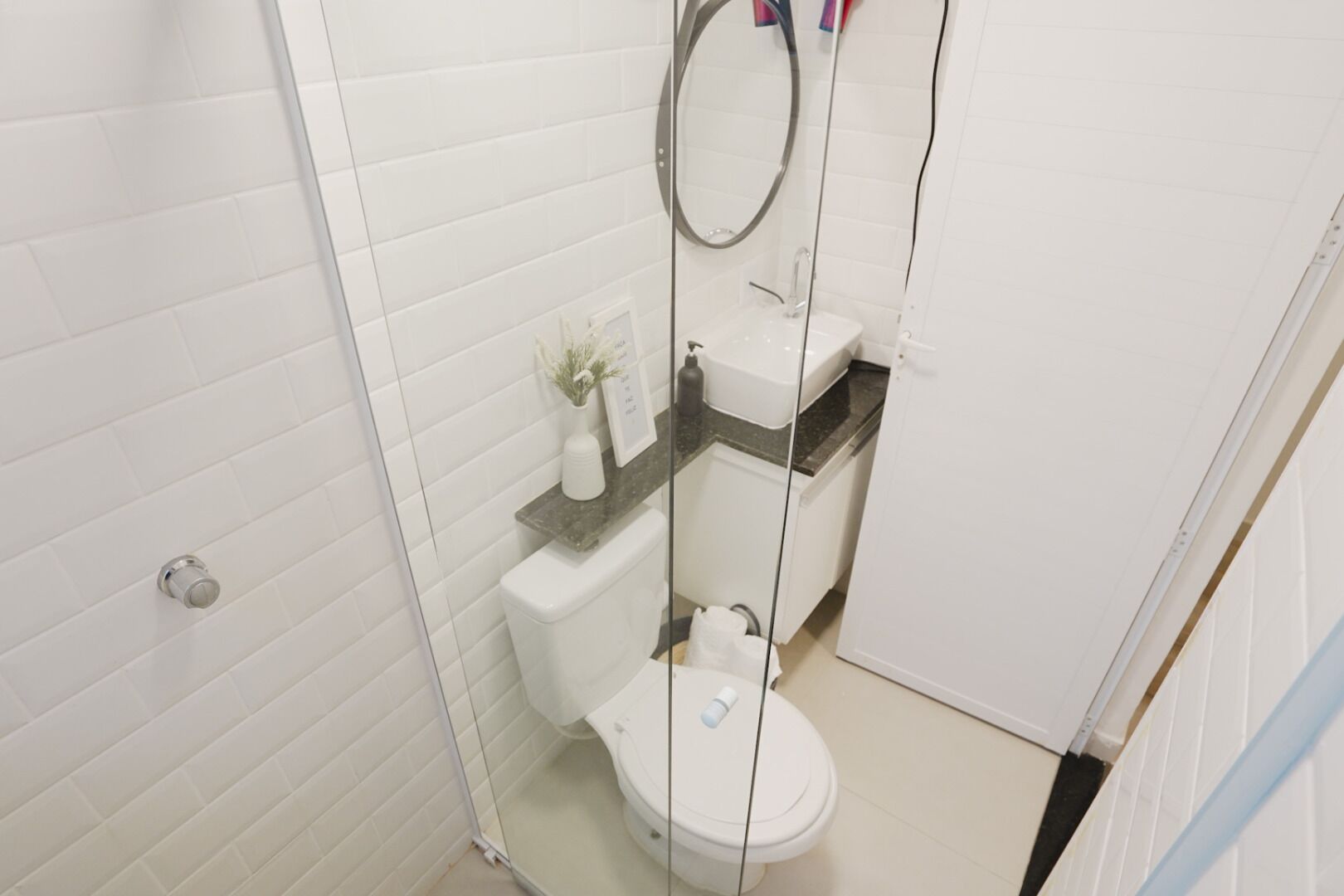 A small, modern bathroom with white tiled walls, a white toilet, a sink with a marble countertop, and a mirror above the sink.