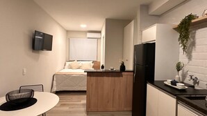 Een kleine keuken met een centraal eiland, een eettafel en een bed op de achtergrond.