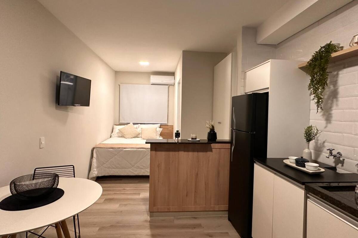 Eine kleine Küche mit einer zentralen Kochinsel, einem Esstisch und einem Bett im Hintergrund.