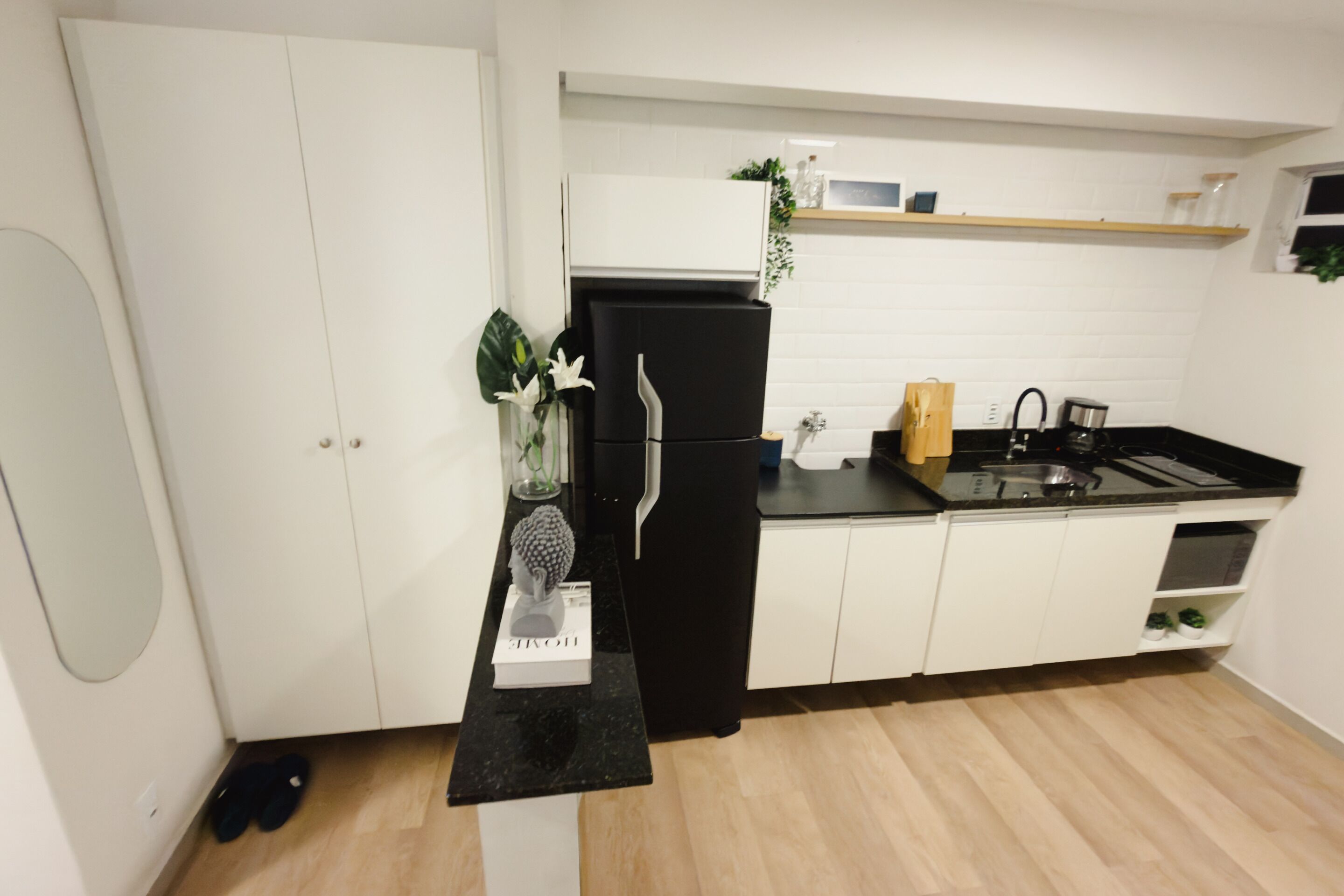 Une cuisine moderne avec des meubles blancs, un réfrigérateur noir, un plan de travail noir et un plancher en bois.