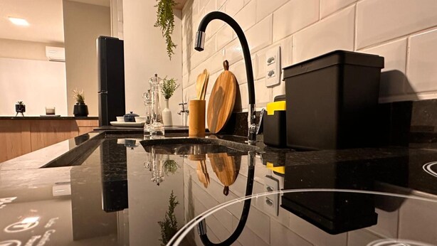 Een moderne keuken met een zwart aanrecht, een zwarte kraan en een houten snijplank.