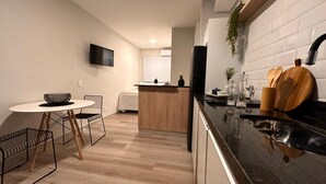 Een moderne keuken met een centraal eiland, een eethoek met een ronde tafel en stoelen, en een aan de muur bevestigde televisie.