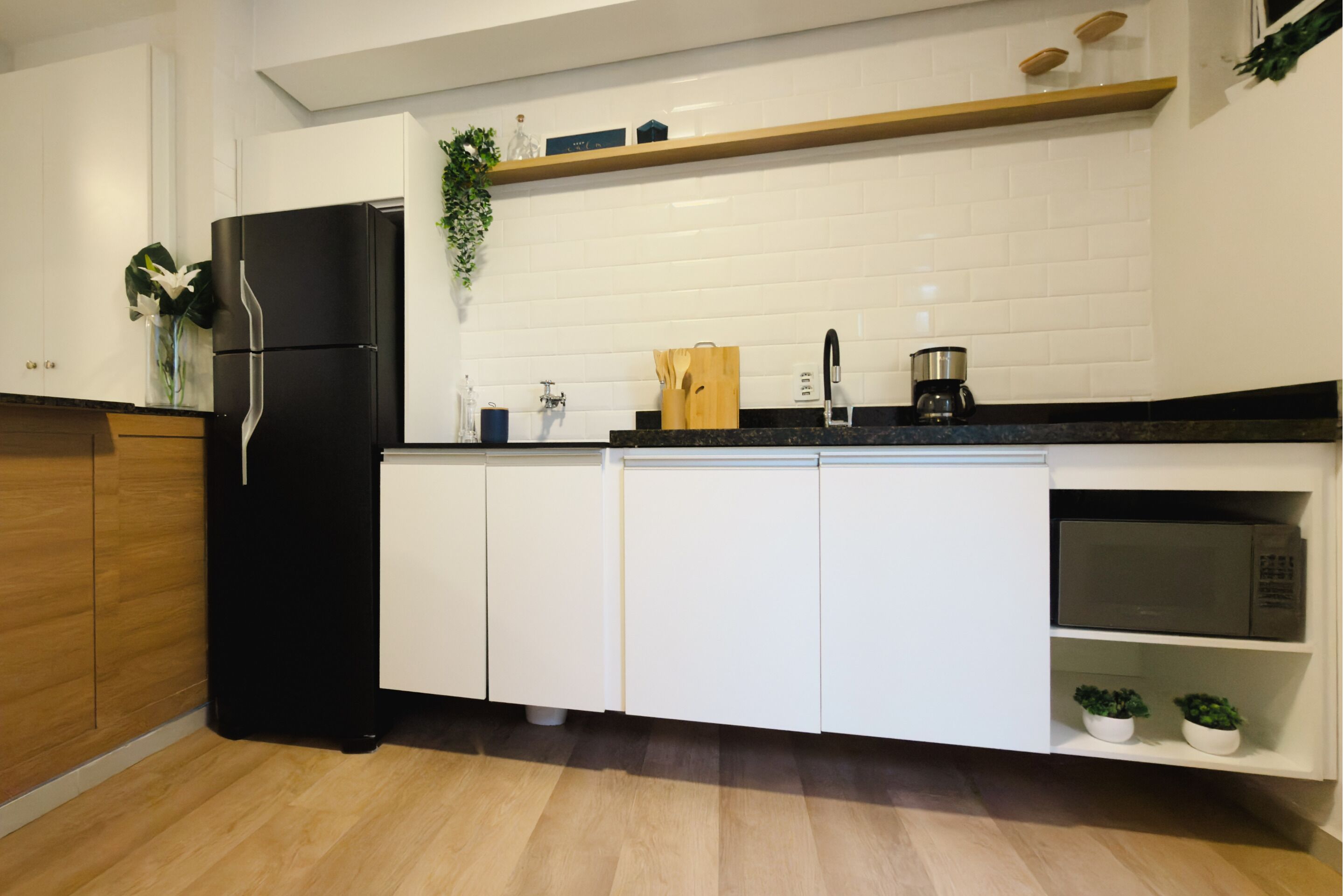 A modern kitchen with a black refrigerator, white cabinets, a wooden countertop, and a microwave.