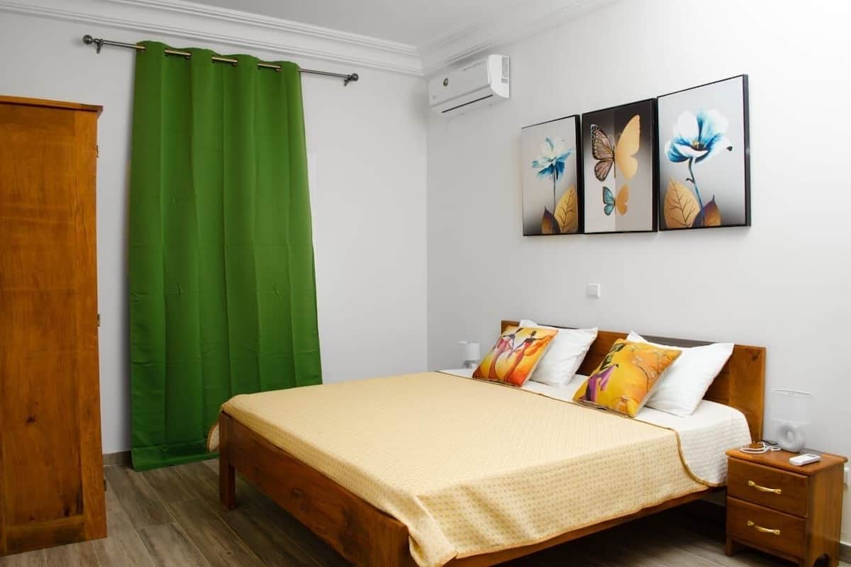 Un dormitorio con cama de madera, cortinas verdes y tres cuadros de flores colgados en la pared.
