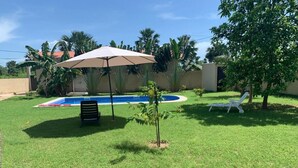 A backyard with a swimming pool, a covered seating area, and a small tree. - Cap Skirring (Cap Skirring)