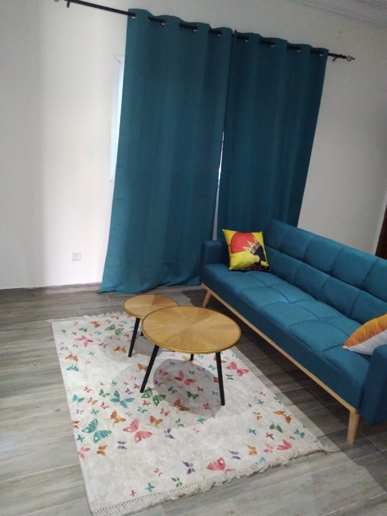 A living room with a blue sofa, two round wooden tables, a colorful rug, and a curtain.
