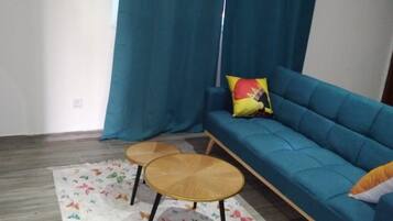 A living room with a blue sofa, two round wooden tables, a colorful rug, and a curtain.