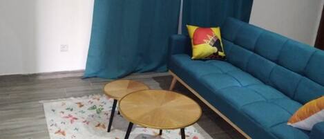A living room with a blue sofa, two round wooden tables, a colorful rug, and a curtain.