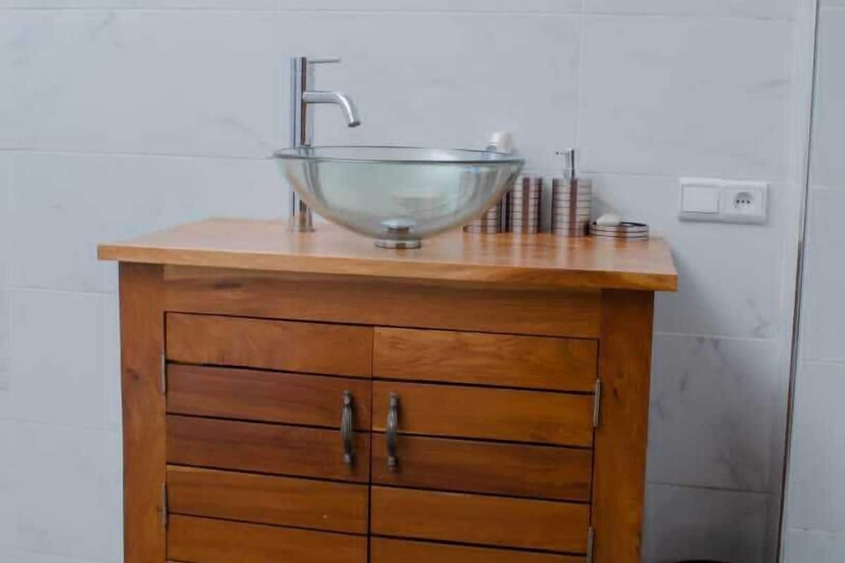 Un baño con tocador de madera, lavabo de cristal y espejo superior.