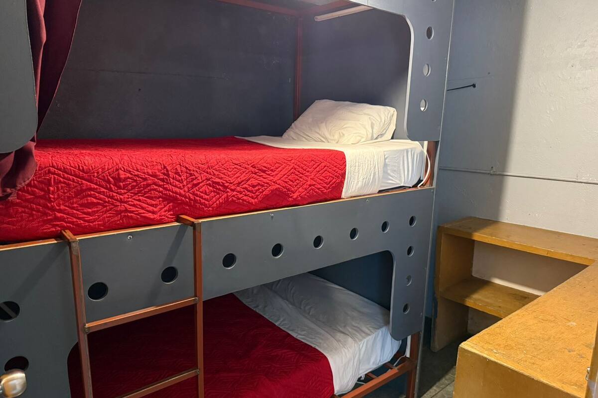 Ein Stockbett mit einer roten gesteppten Matratze und einem weißen Kopfkissen.