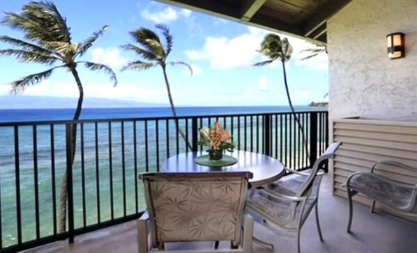 A balcony with a view of the ocean, a round table with chairs, and a potted plant.