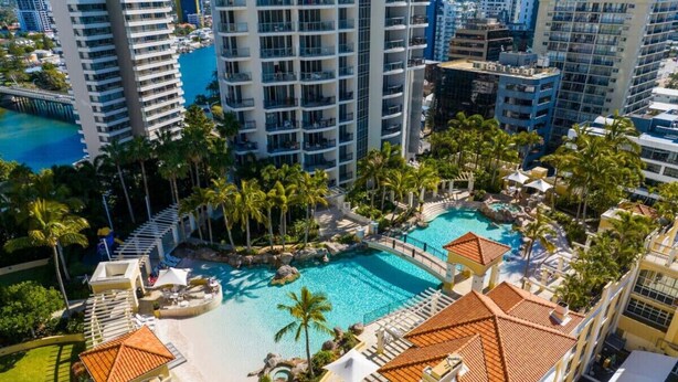 A resort with a large pool, palm trees, and high-rise buildings in the background. - Surfers Paradise: Family Fun w/ 3 Pools, Gym & Spa (Surfers Paradise)