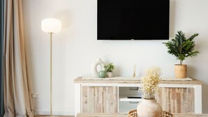 A modern living room with a flat-screen TV mounted on the wall, a floor lamp, a wooden coffee table with decorative items, and a potted plant. - Surfers Paradise: Family Fun w/ 3 Pools, Gym & Spa (Surfers Paradise)