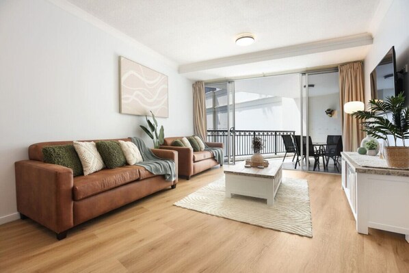 A modern living room with a brown leather sofa, a white coffee table, and a dining area with a white cabinet and a plant.