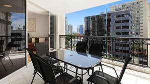A balcony with a glass door leading to a living area, a dining table with chairs, and a view of surrounding high-rise buildings. - Surfers Paradise: Family Fun w/ 3 Pools, Gym & Spa (Surfers Paradise)