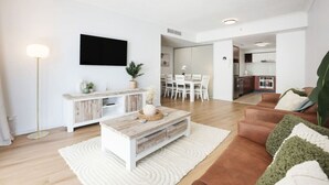 A modern living room with a sofa, coffee table, and a TV mounted on the wall. There is a dining area with a table and chairs visible in the background. - Surfers Paradise: Family Fun w/ 3 Pools, Gym & Spa (Surfers Paradise)