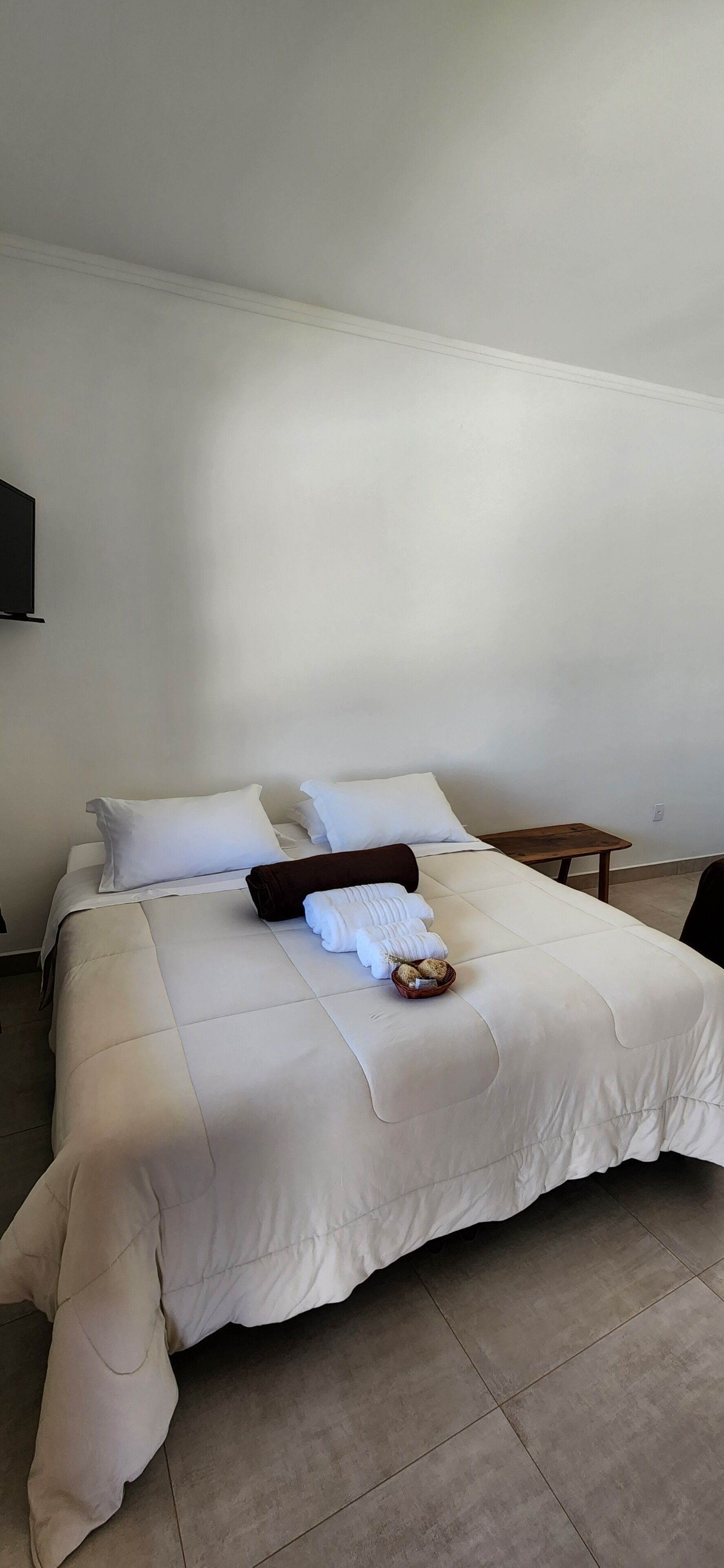 Una cama bien tendida con un edredón blanco, una manta marrón y una cesta de pan.