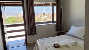 A bedroom with a bed, an air conditioning unit, a window with curtains, and a view of the outdoors. - Pousada Luz de Candeia (São João Batista do Glória)