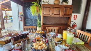 A wooden dining table set with various dishes, a wooden cabinet, and a wall-mounted plant. - Pousada Luz de Candeia (São João Batista do Glória)