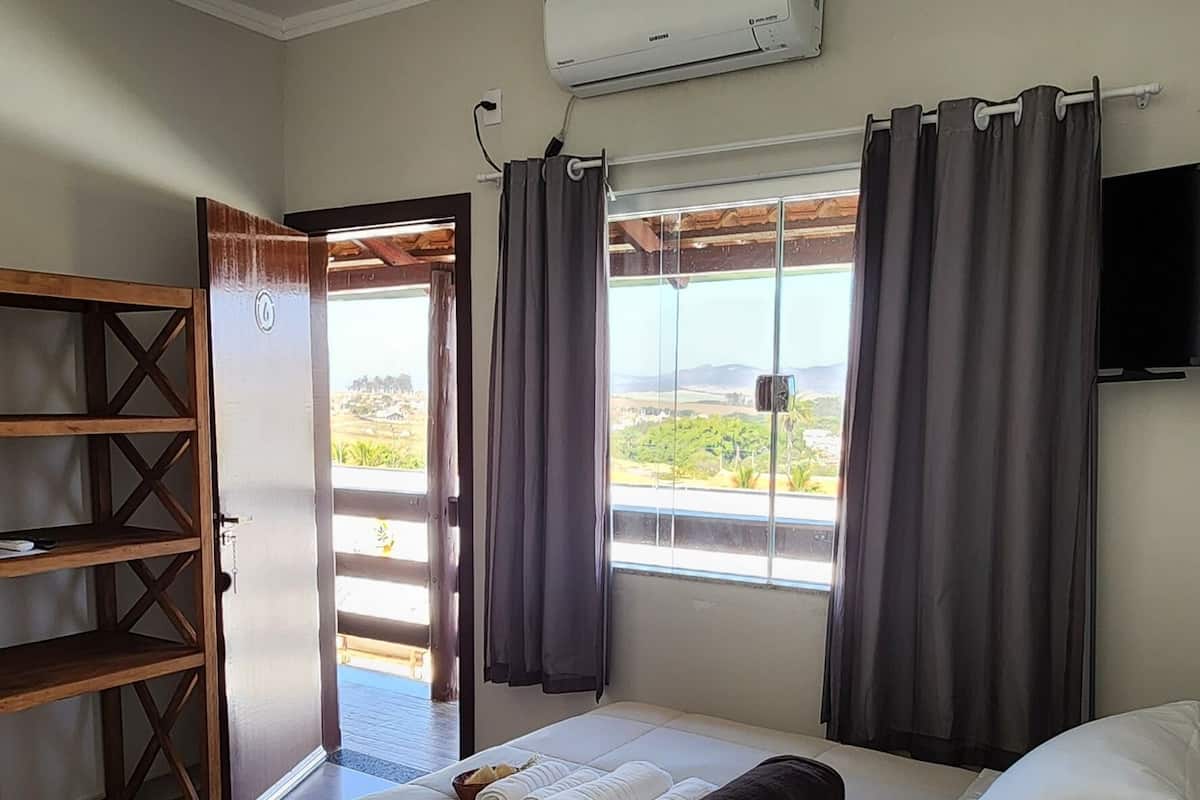 Une chambre d’hôtel avec un lit, une étagère en bois, un appareil de climatisation et une vue sur l’extérieur.