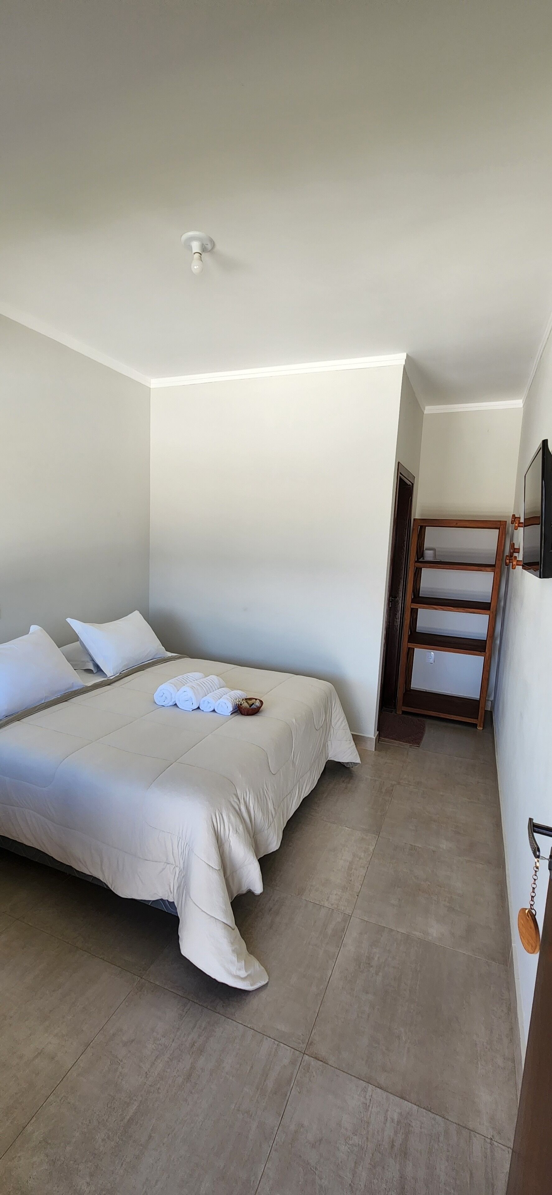 A neatly made bed with rolled towels and pillows, a wooden ladder, and a small wooden shelf.