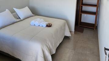 A neatly made bed with rolled towels and pillows, a wooden ladder, and a small wooden shelf.